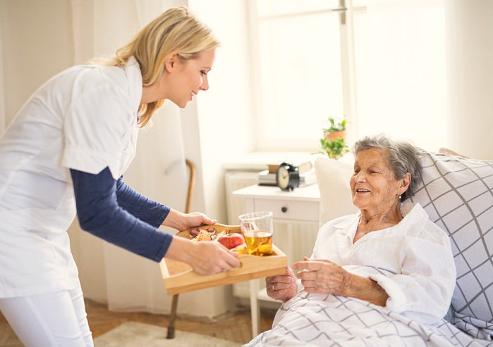 caregiver serving senior woman her meal on her bed